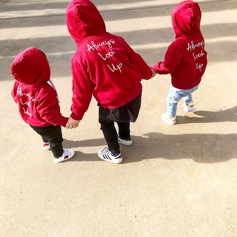 Three children wearing THE UNKNOWN CHILDREN 'Originals' "Always Look Up" red hoodies,
walking hand in hand. This unisex, limited-edition hoodie is made from 100% superior cotton,
showcasing a trendy and comfortable design for boys and girls.