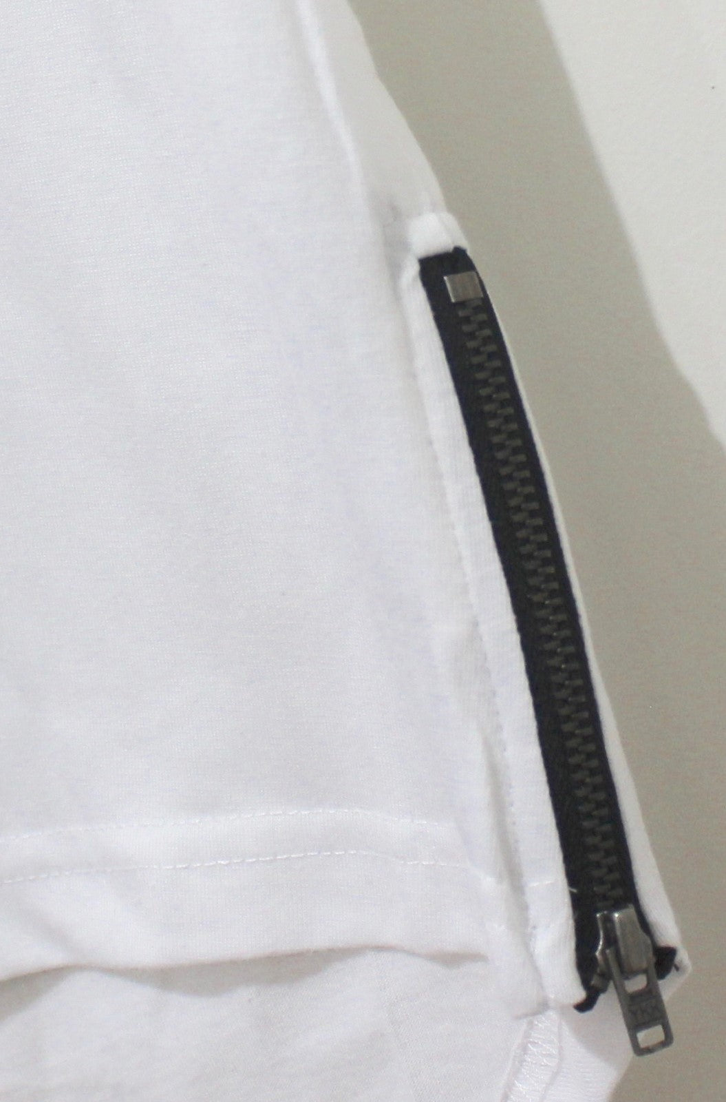 Close-up view of the zip detail on THE UNKNOWN CHILDREN Zipped Curved Tee in white. This stylish tee, made from 100% superior cotton, features a unique side zipper design, adding a modern and functional touch to the curved hem. Ideal for fashion-forward kids.