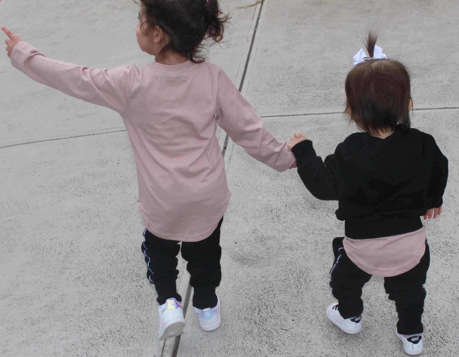 Two children holding hands on a concrete surface wearing pink long sleeve tees