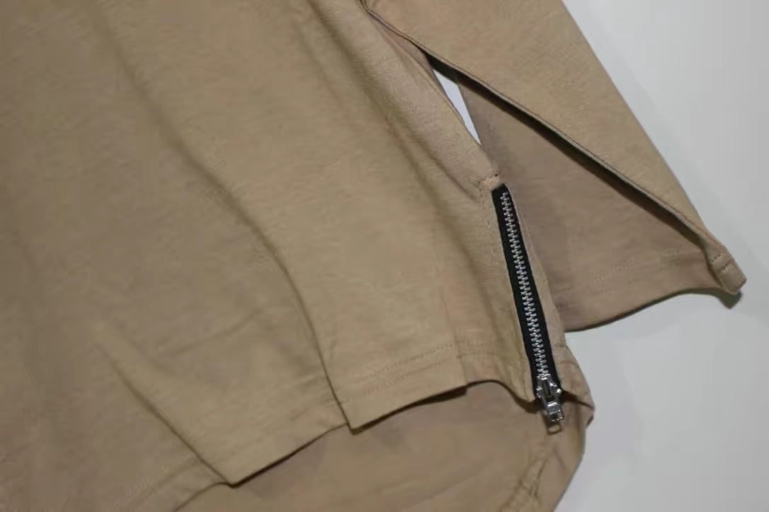 Close-up of the beige curved hem tee from THE UNKNOWN CHILDREN, featuring a stylish side zipper. Made from 100% superior cotton, this tee offers both comfort and a modern design for everyday wear.