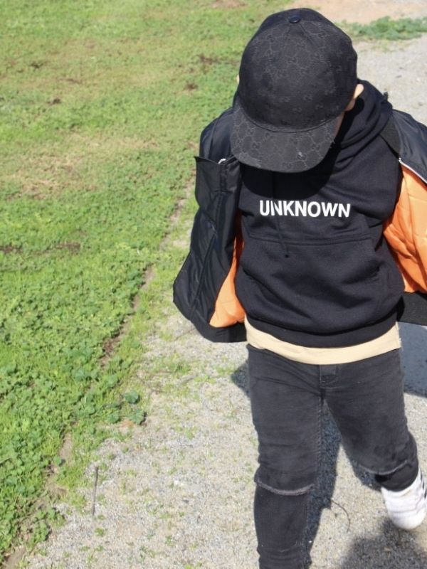 Child wearing a black "UNKNOWN" hoodie paired with The Black Bomber Jacket, black Jeans, and a 
matching black cap. The stylish and warm outfit is perfect for casual outdoor play.