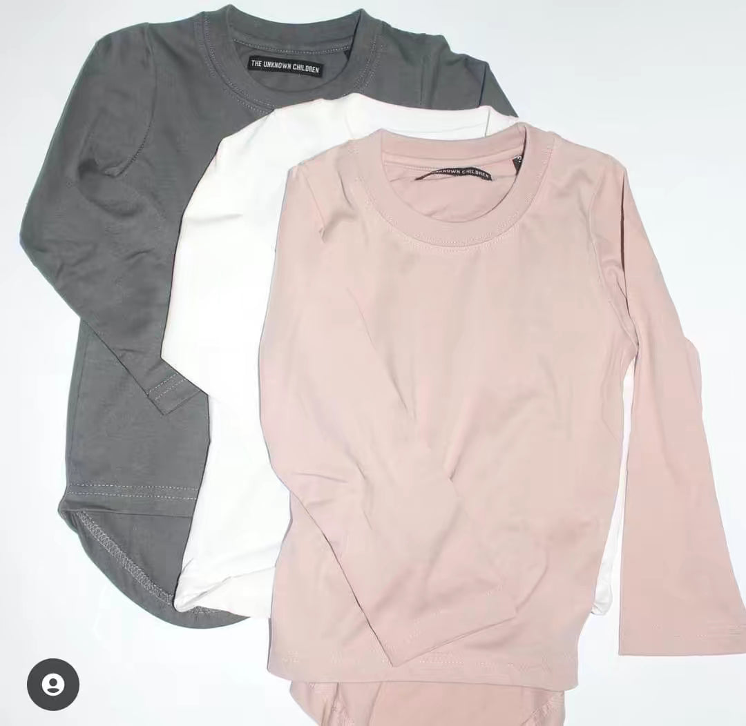 Three long-sleeve curved hem t-shirts from THE UNKNOWN CHILDREN in gray, white, and blush pink, made from 100% superior cotton. These stylish and breathable tees offer a modern and comfortable fit for everyday wear.