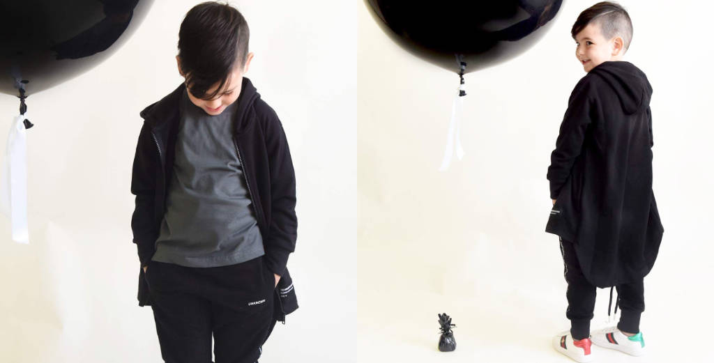 Child wearing a black jacket and gray shirt with black balloons in the background